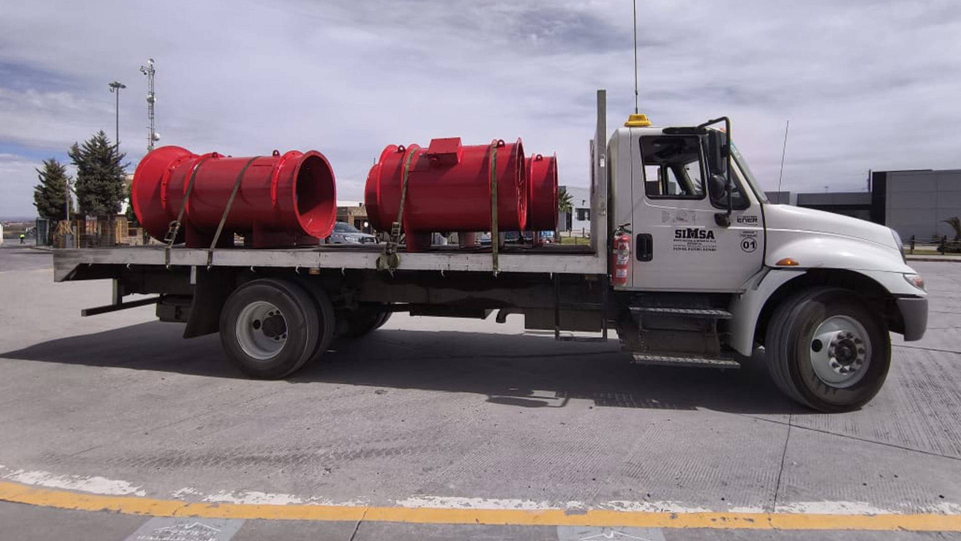 Vista lateral de un camión de carga SIMSA transportando dos ventiladores industriales de color rojo brillante para aplicaciones de minería o túneles.