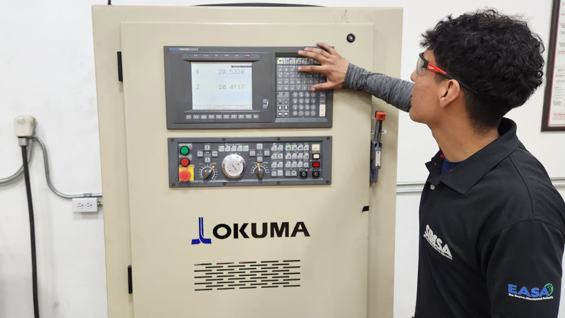 Ingeniero verificando parámetros operativos y tolerancias en un panel de control CNC Okuma tras la reparación.