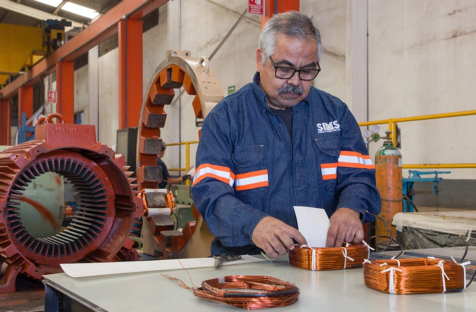 Técnico calificado realizando el proceso de aislamiento y preparación de bobinas para el rebobinado de un estator industrial.