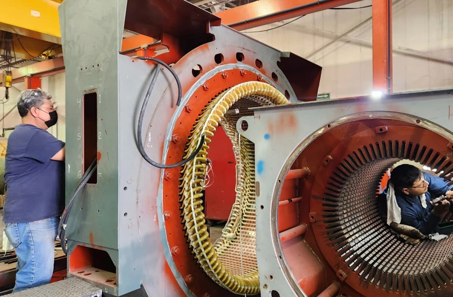 Técnicos calificados realizando el rebobinado manual de un estator para motor eléctrico de gran escala.