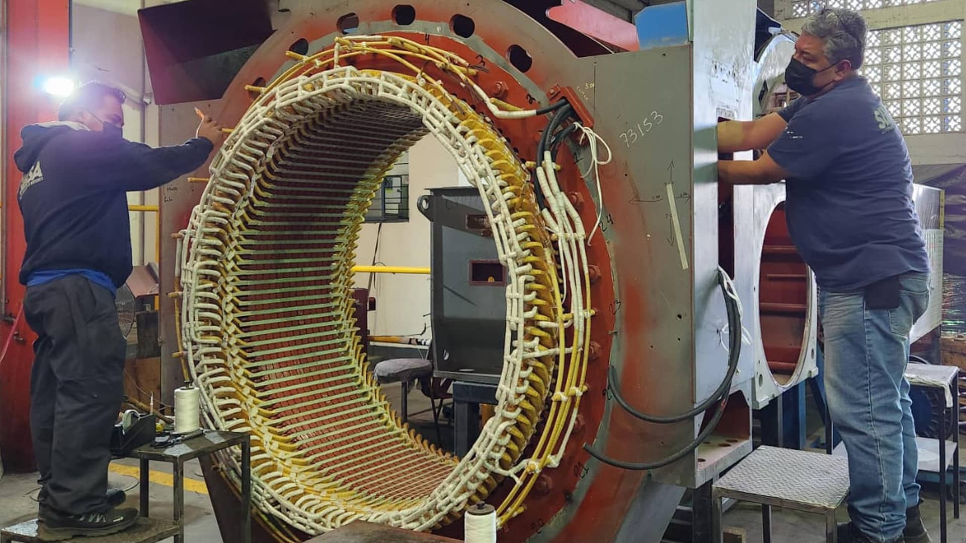 Técnicos especializados realizando el rebobinado y aislamiento manual de un estator de gran tamaño.