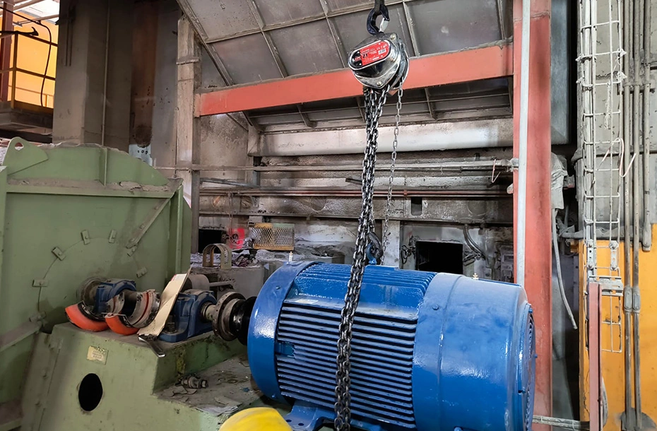 Maniobra de izaje y posicionamiento de motor eléctrico industrial mediante polipasto de cadena durante servicio de instalación.