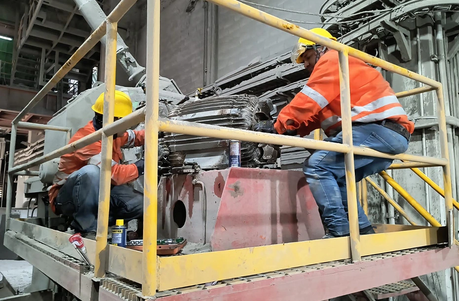 Equipo de ingenieros de campo realizando ajustes mecánicos y fijación en la base de un motor eléctrico industrial.